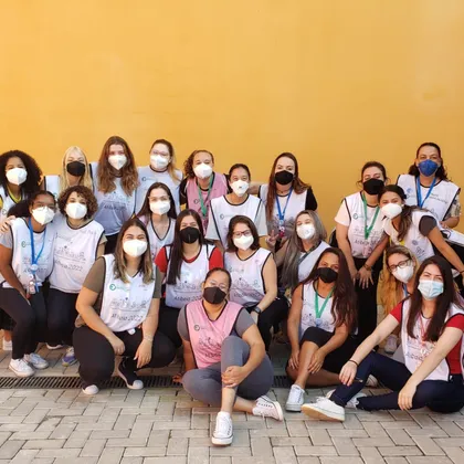 Equipe grande de estudantes de colete diante de um muro amarelo