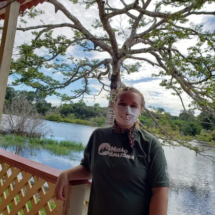 Luciene de máscara em uma varanda à beira do rio