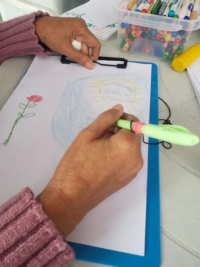 Mãos de uma senhora escrevendo com caneta adaptada