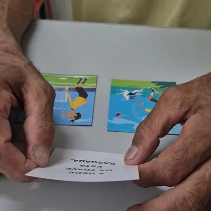 Mãos segurando um cartão com uma frase e duas cartas ilustradas