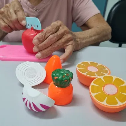 Mãos de uma senhora cortando uma maçã de brinquedo