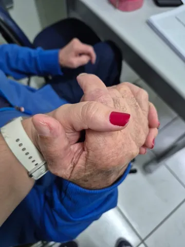Mão da fonoaudióloga segurando a mão de um senhor idoso