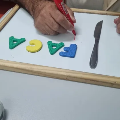 Paciente escrevendo em um quadro com a palavra FACA em letras de EVA, ao lado de uma faca